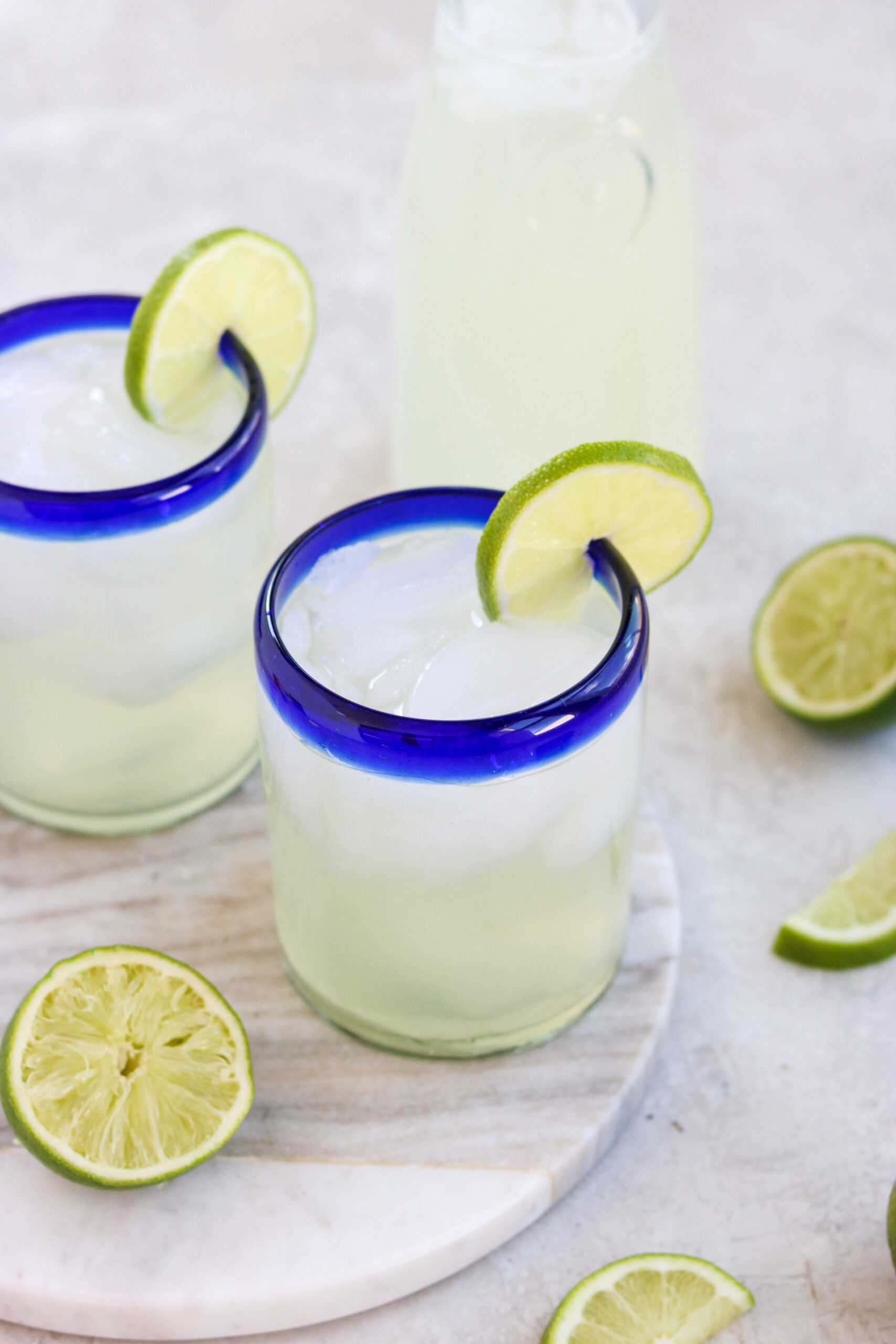 two glasses filled with lime juice, water, and honey with a lime wedge on the rim and a half of a squeezed lime next to the glasses. 