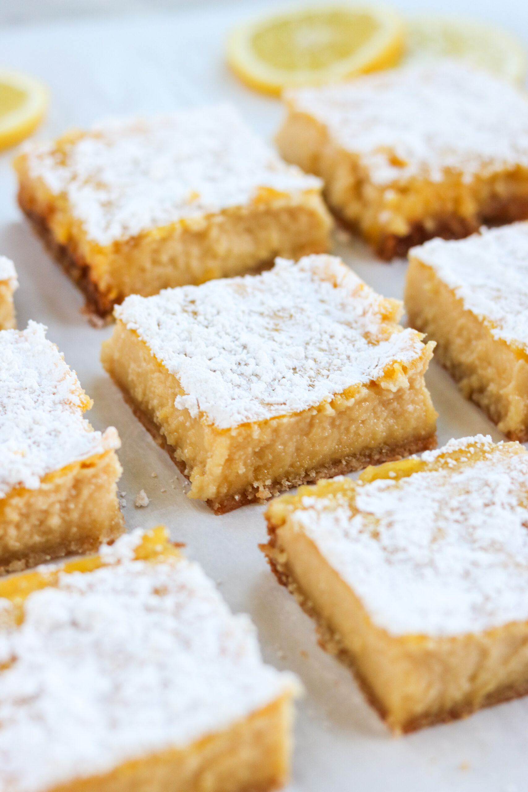 a close up of gluten free lemon bars in a row dusted with powdered sugar