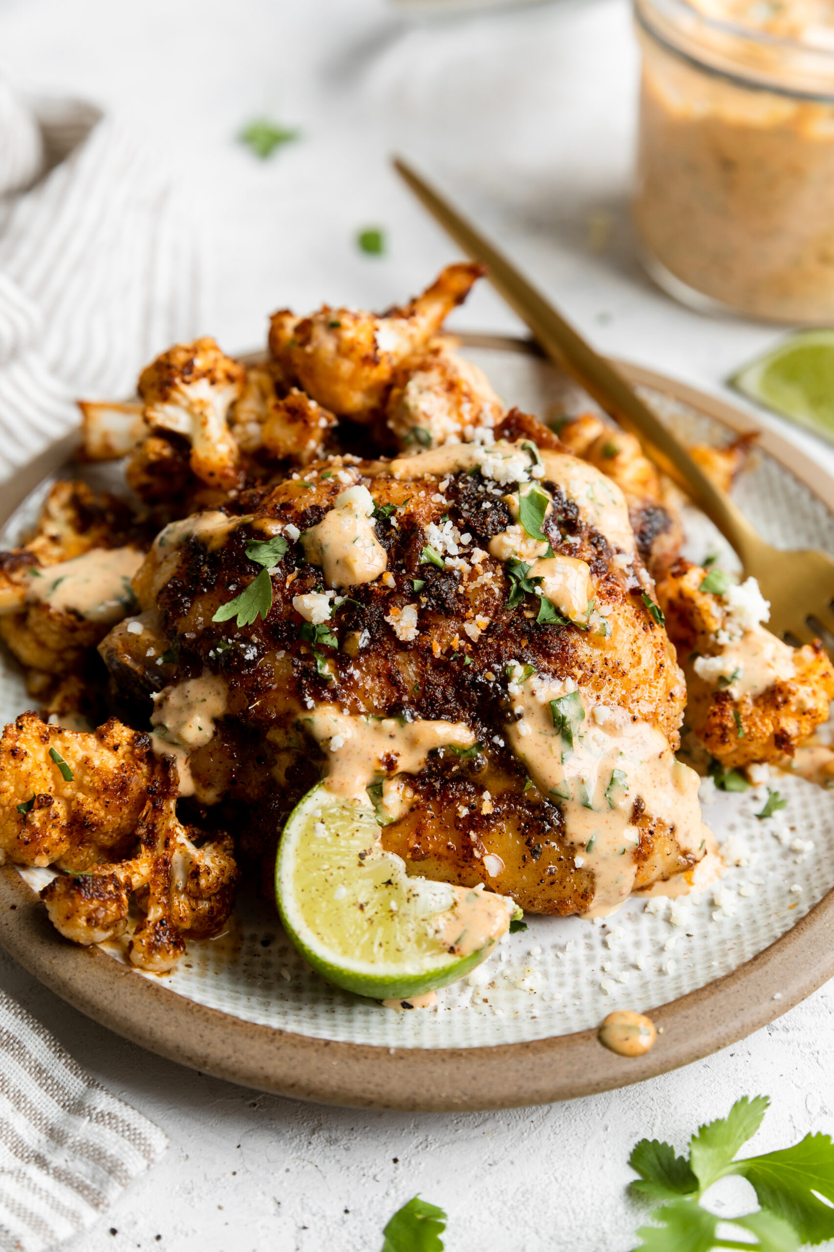 a close of up the roasted cauliflower and crispy chicken thighs next to a lime wedge and a bowl of sauce