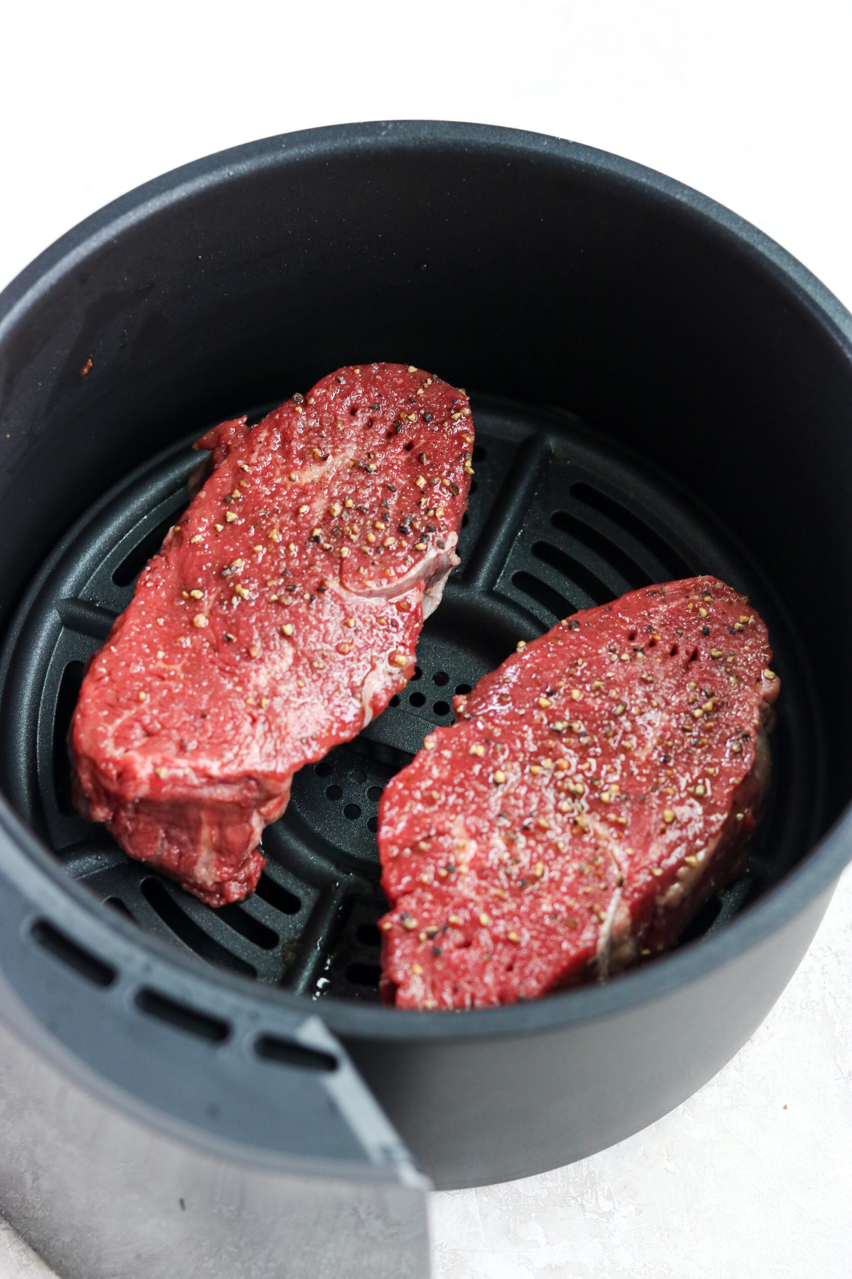 two seasoned raw steaks in air fryer basket 