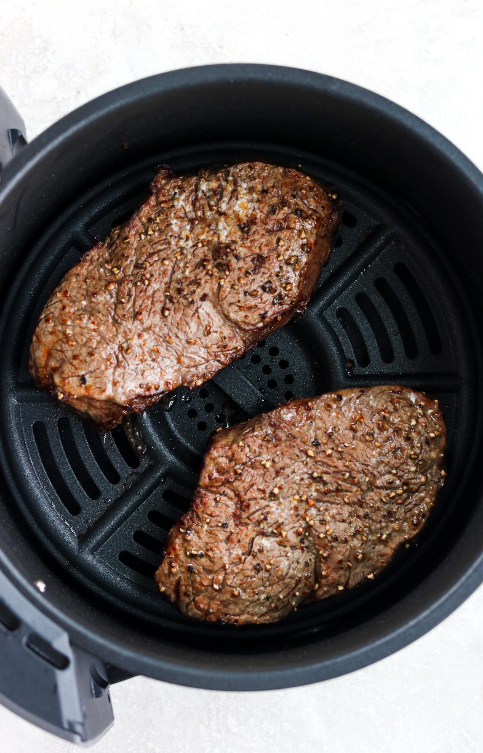 two cooked steaks in air fryer basket