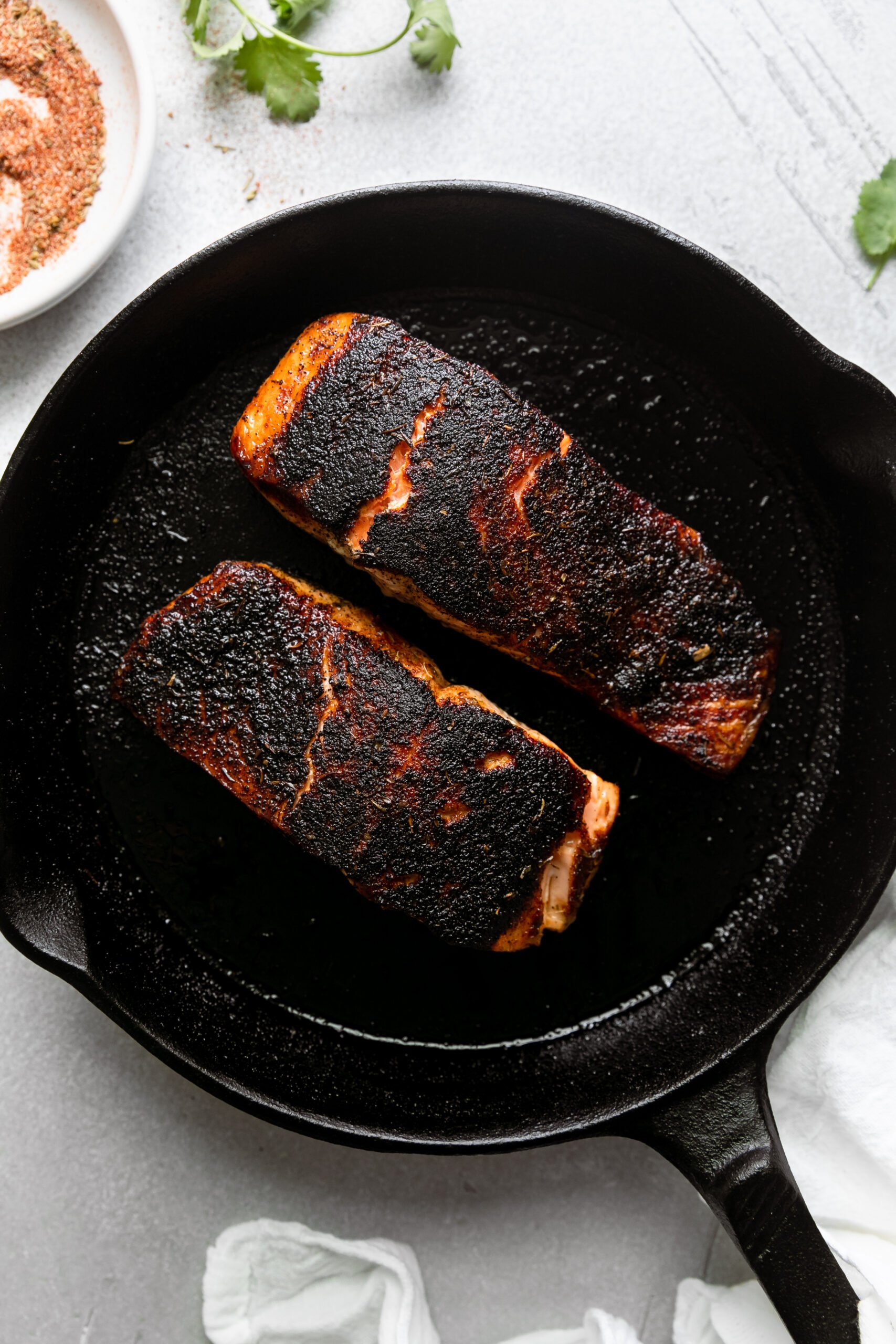 a cast-iron skillet with two pieces of blackened salmon cooking.