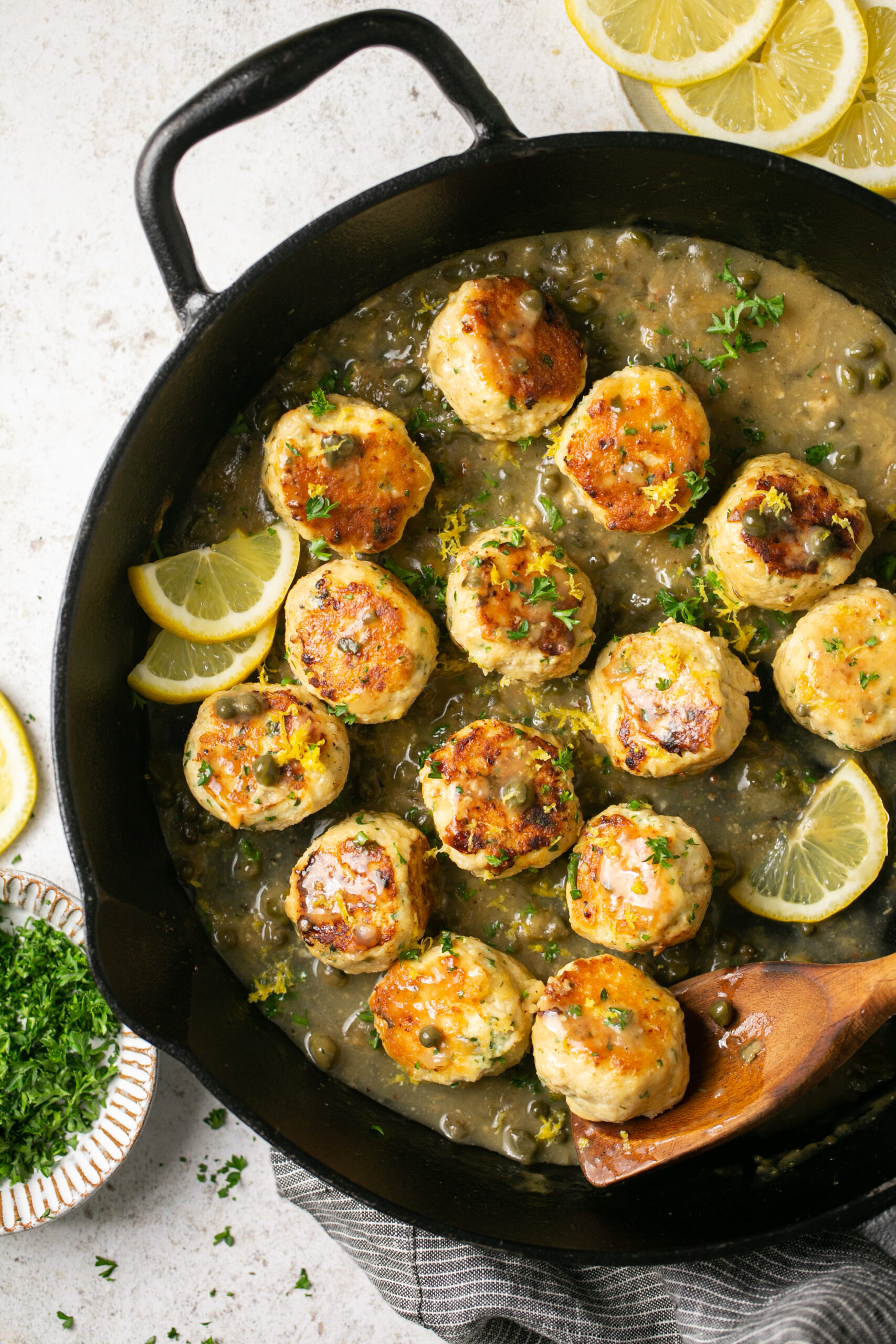 a skillet with chicken piccata meatballs with lemon as garnish