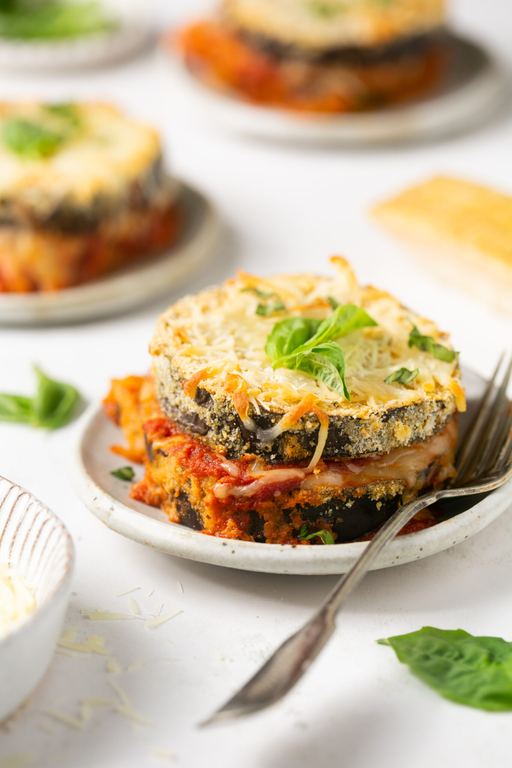 3 individual servings of keto eggplant parmesan on white plates with a silver fork