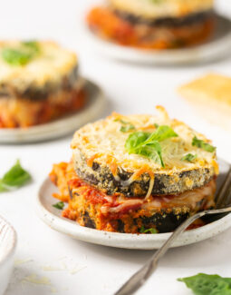 3 servings of baked eggplant parmesan on white plates with a silver fork
