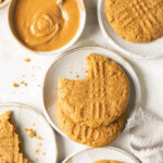 gluten free peanut butter cookies on small white plates with a bowl of creamy peanut butter and a white napkin