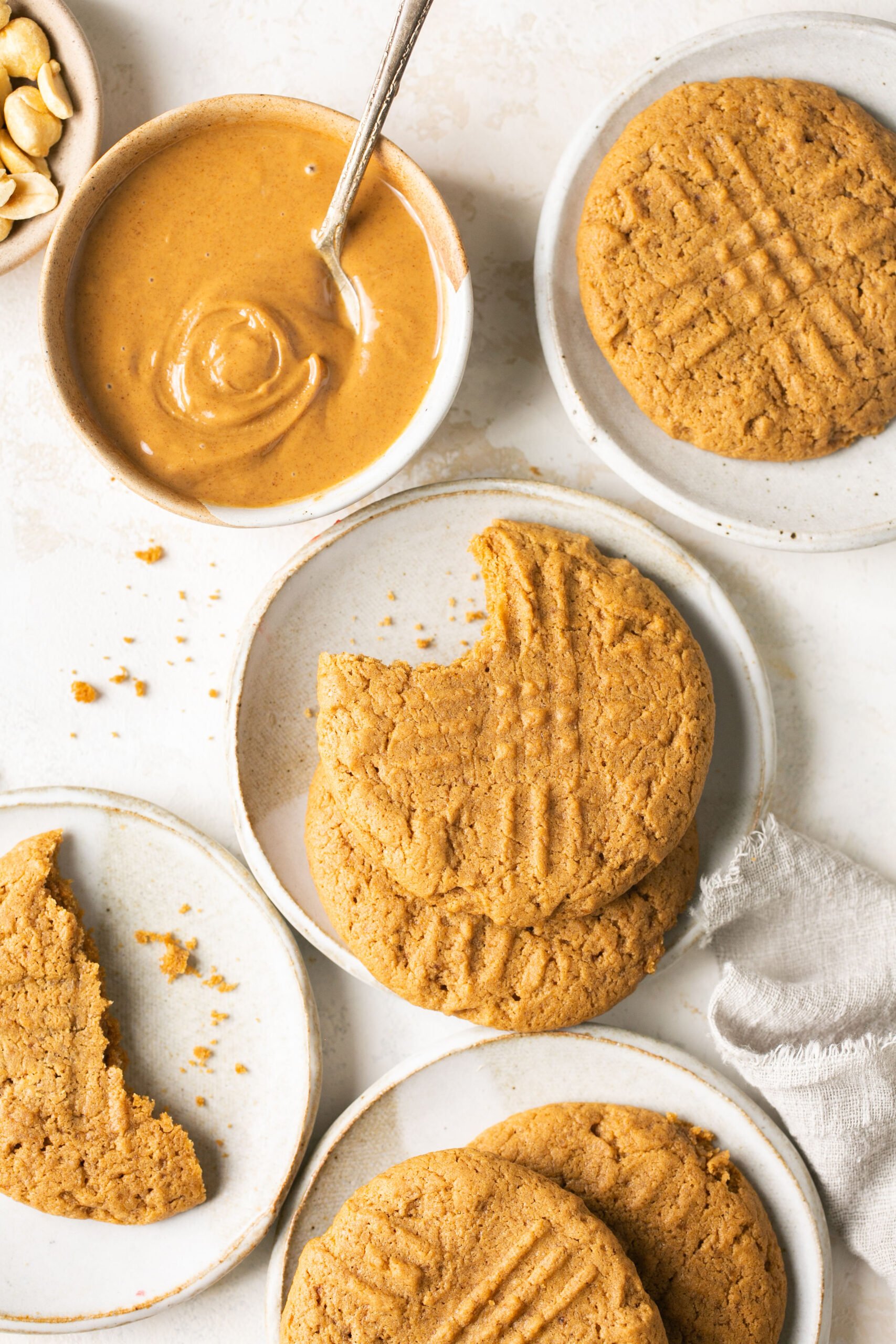 cookies on small white plates with a bowl of creamy peanut butter and a white napkin
