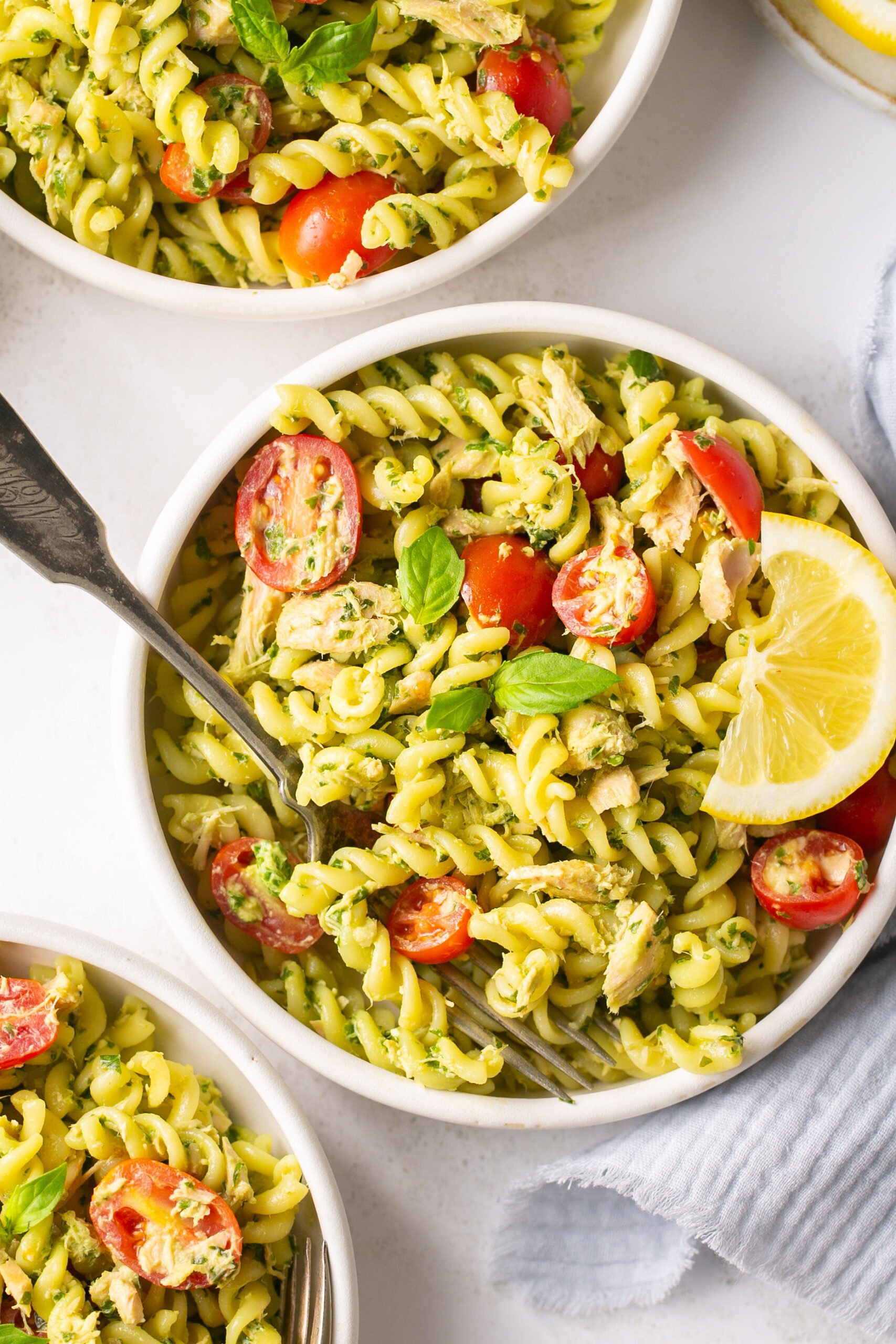 a closeup shot of three white bowls filled with pesto pasta and tomatoes. 