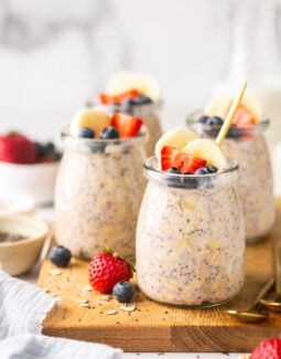 protein overnight oats in mini glass jars on a wooden cutting board topped with fruit