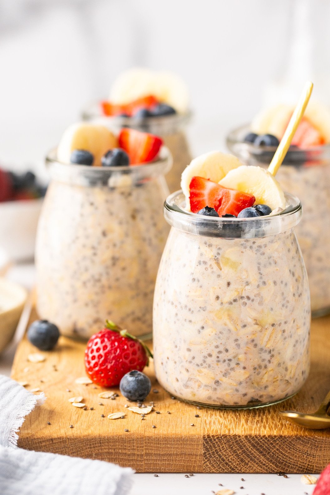 overnight oats in small jars topped with fruit on a wooden cutting board