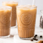 mocha iced coffee in a glass with a straw with coffee beans on the side