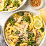 sausage broccolini pasta with penne in 2 white bowls with a nesting bowl full of crushed red pepper