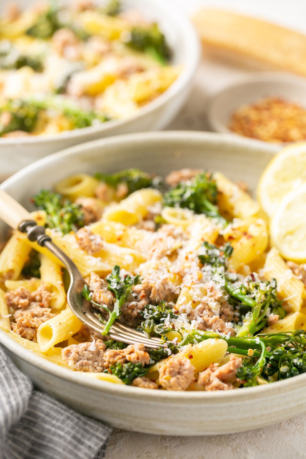 sausage broccolini pasta in a white bowl with lemon