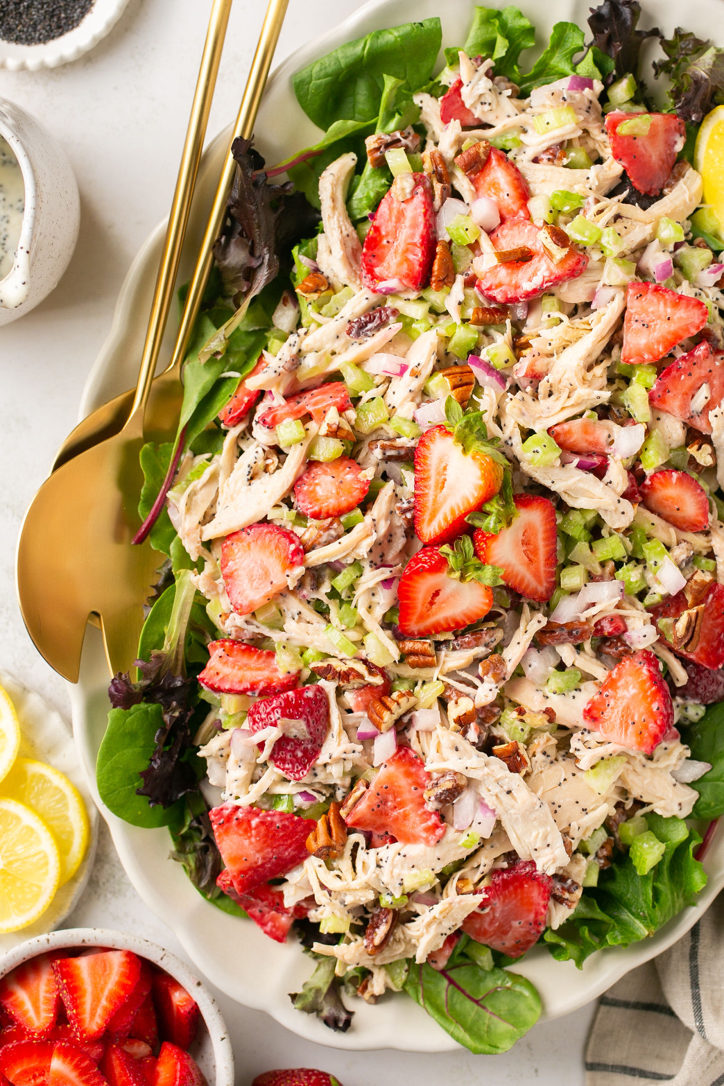 strawberry poppyseed chicken salad on a platter with gold serving spoons and greens