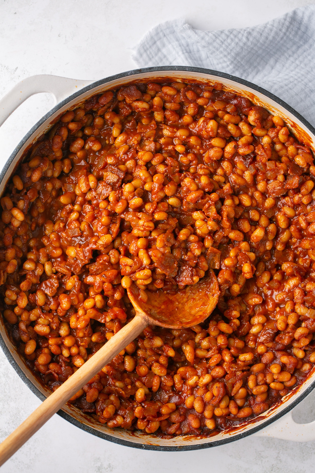 a pot of baked beans with a towel underneath and a wooden spoon