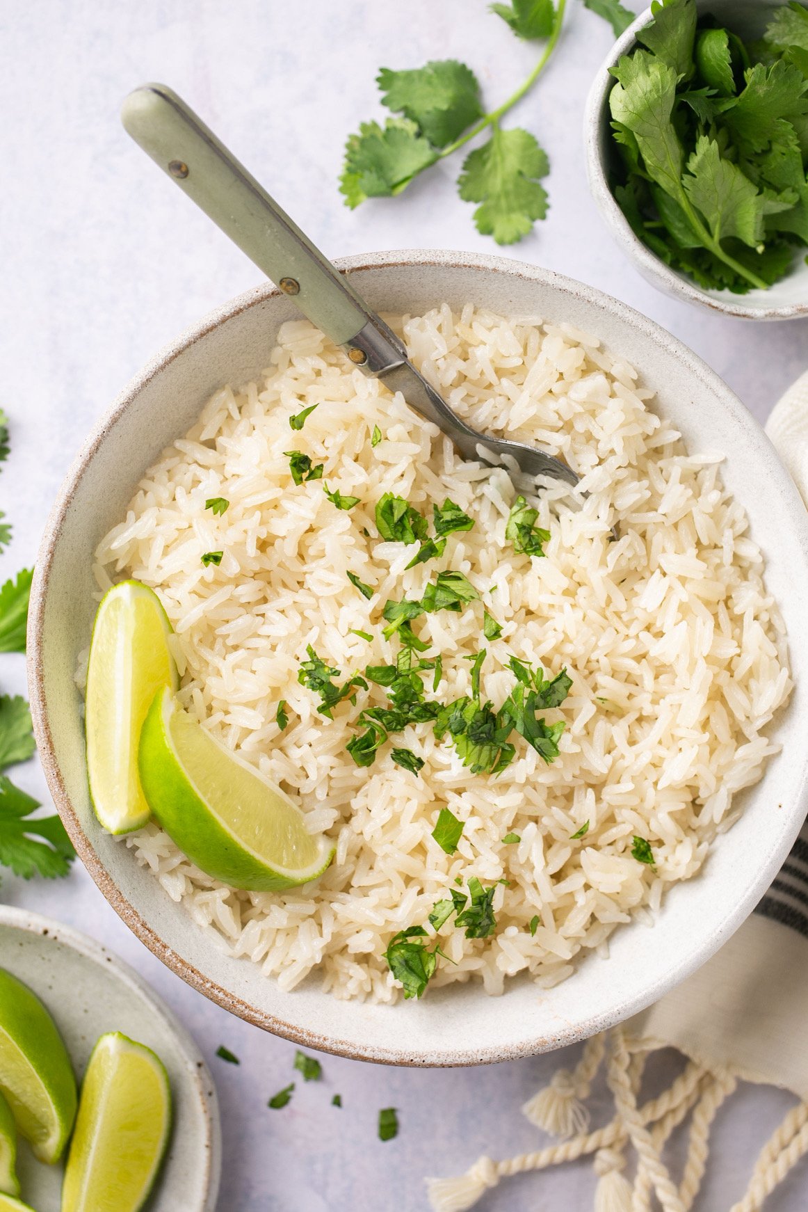 a bowl of instant pot coconut rice topped with chopped cilantro and two lime wedges
