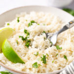 instant pot coconut rice topped with cilantro and a wedge of lime in a white bowl with a silver spoon
