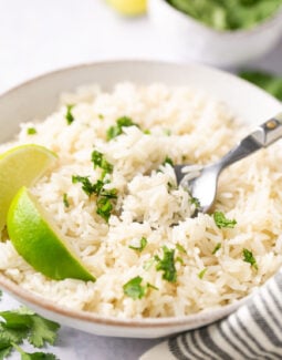 instant pot coconut rice topped with cilantro and a wedge of lime in a white bowl with a silver spoon