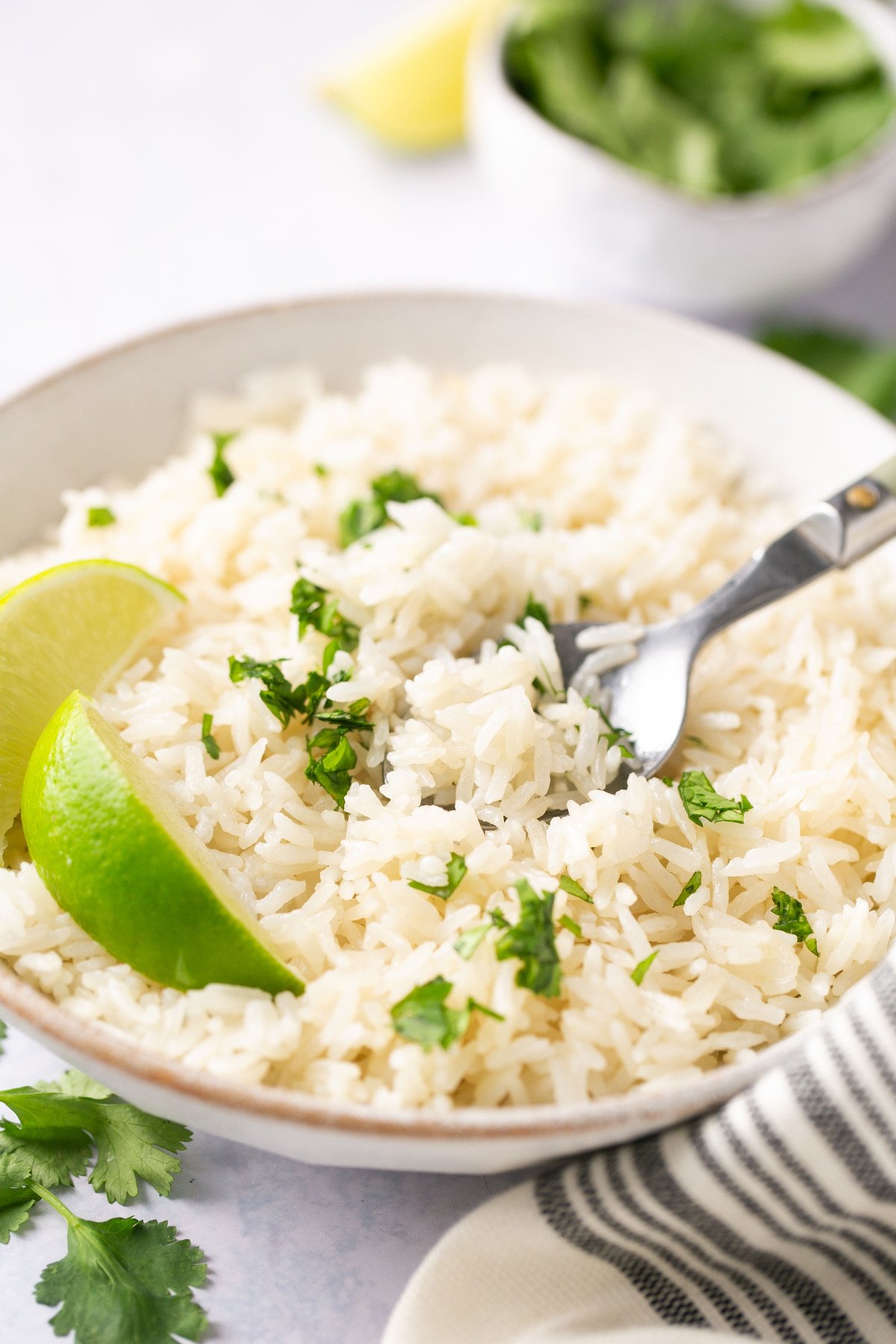 a closeup of coconut rice in a bowl, garnished with lime and cilantro with a silver fork digging into the rice.