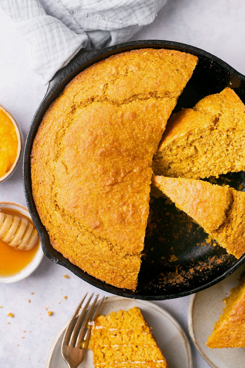 a cast iron pan with slices of sweet potato cornbread next to a white plate with a slice and a silver fork