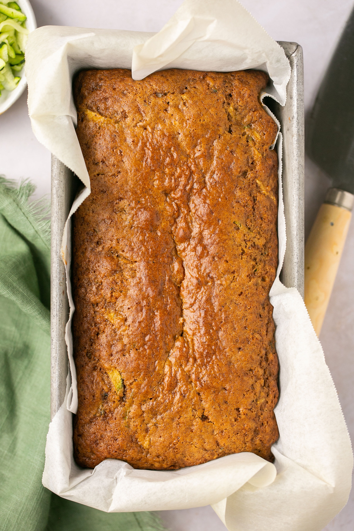 a loaf of gluten free zucchini bread in a metal loaf pan lined with parchment paper