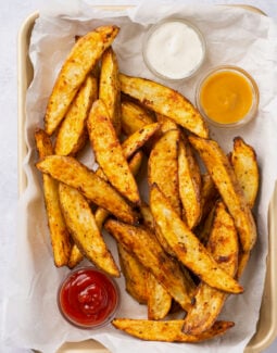 air fryer potato wedges in a basket with 3 dipping sauces