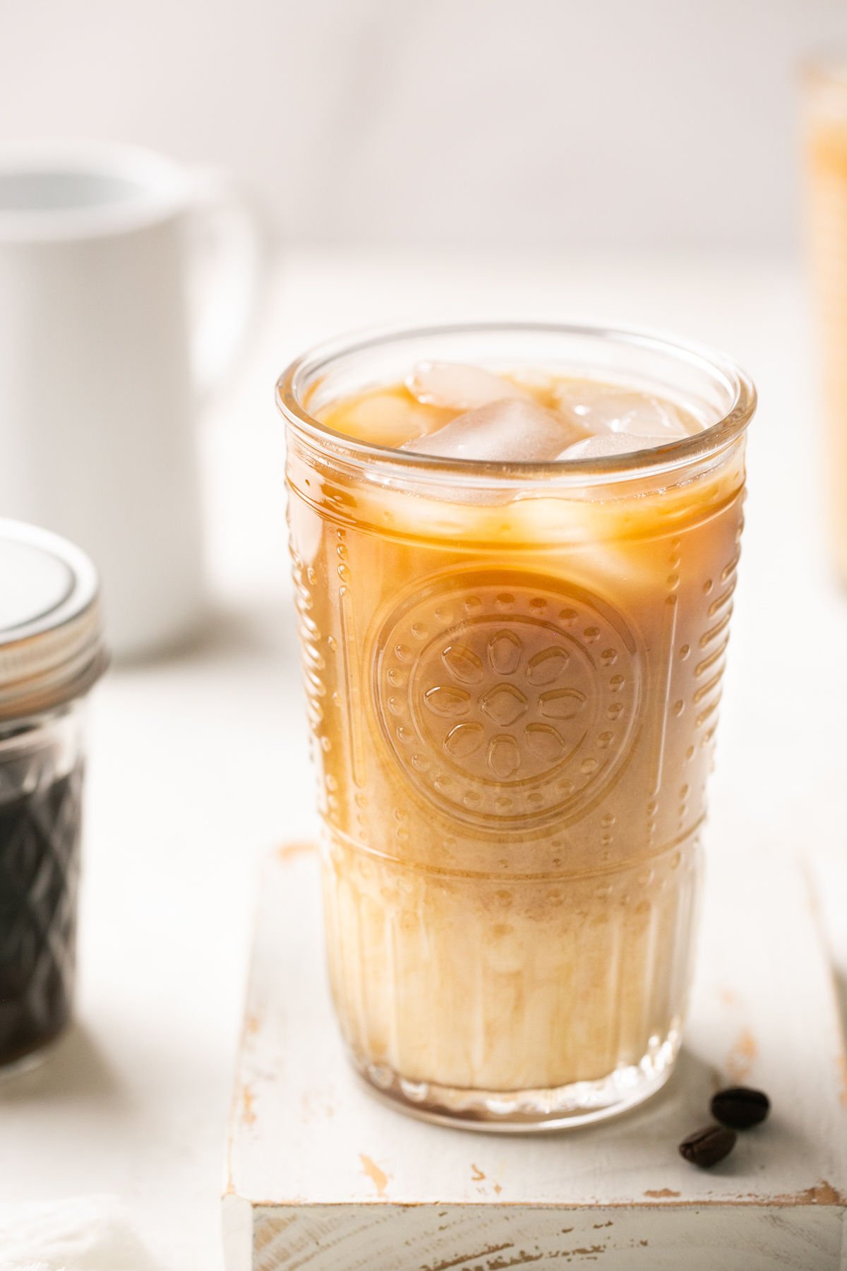 a closeup of a glass of shaken espresso with oatmilk over ice next to a jar of brown sugar syrup