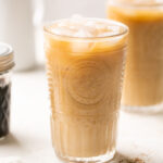 brown sugar shaken espresso in a glass with coffee beans and brown sugar syrup in the background