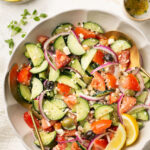 Greek cucumber salad in a bowl with parsley and lemon with a gold spoon