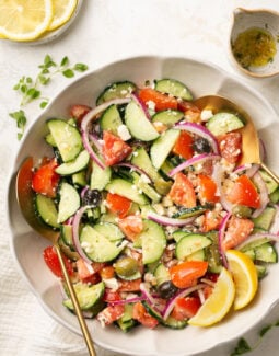 Greek cucumber salad in a bowl with parsley and lemon with a gold spoon