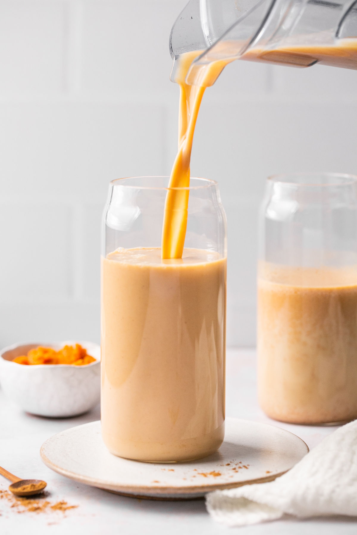 a pitcher pouring iced pumpkin spiced latte ingredients into a glass cup. 