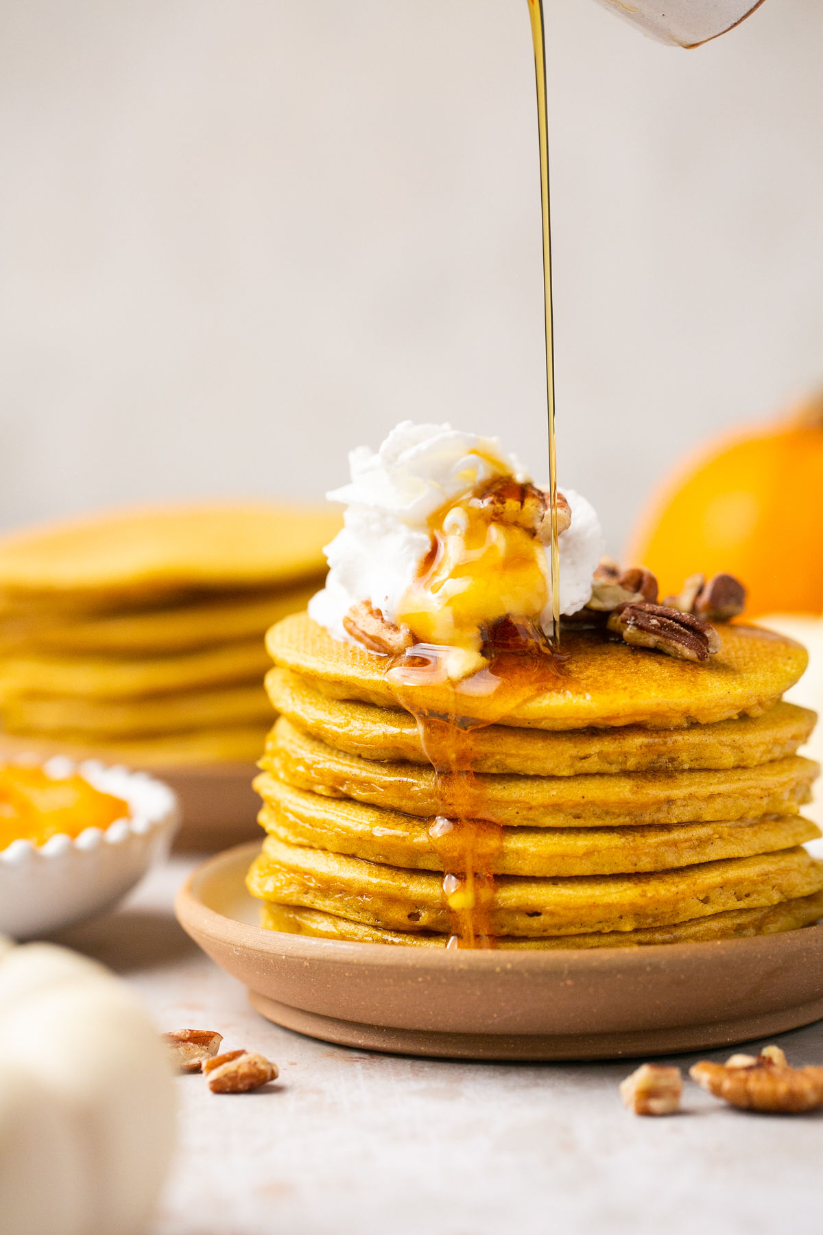 gluten free pumpkin pancakes stacked on a plate topped with pecans, whipped cream, and maple syrup