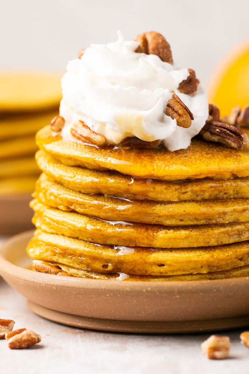 a close up of a stack of pancakes topped with whipped cream and pecans and syrup