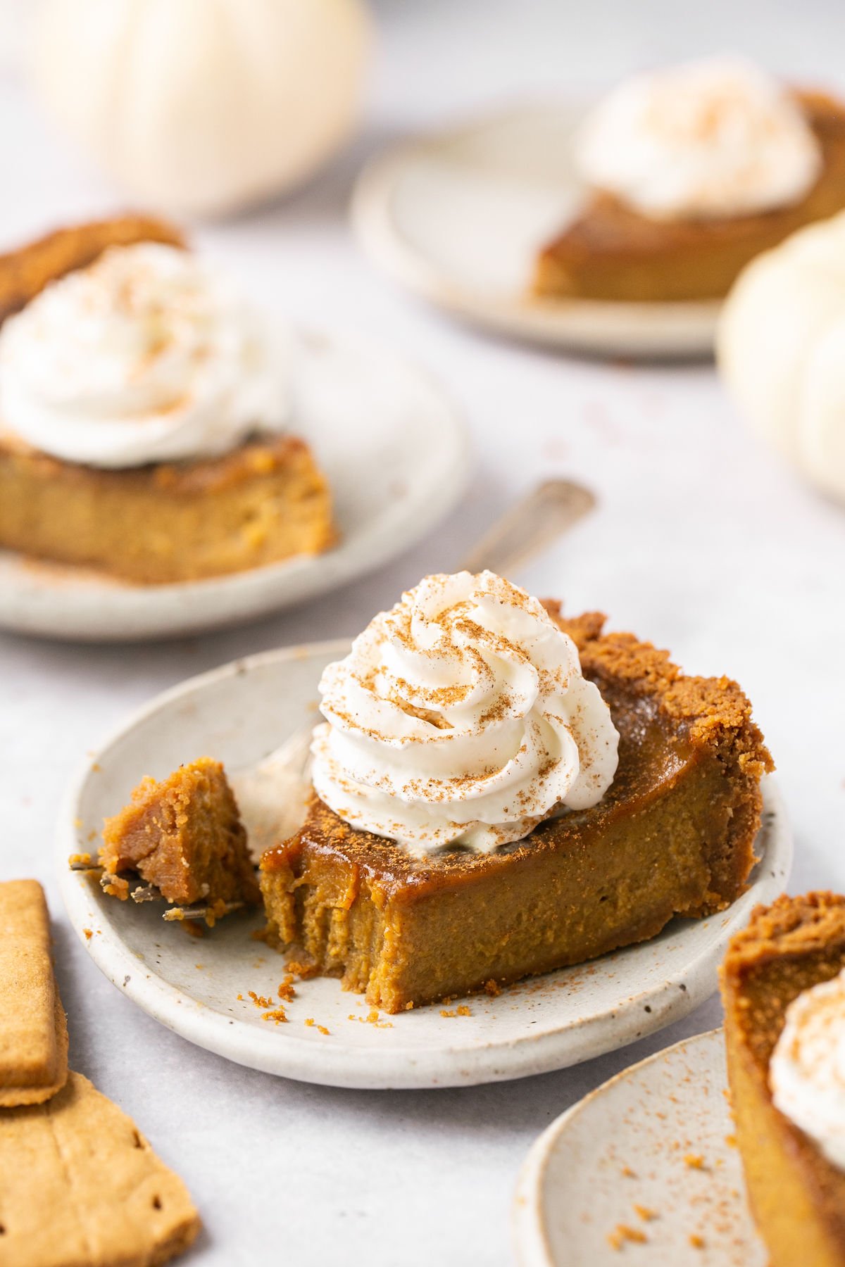 a closeup of a slice of pumpkin pie with a bite taken out on a white plate topped with whipped cream. 