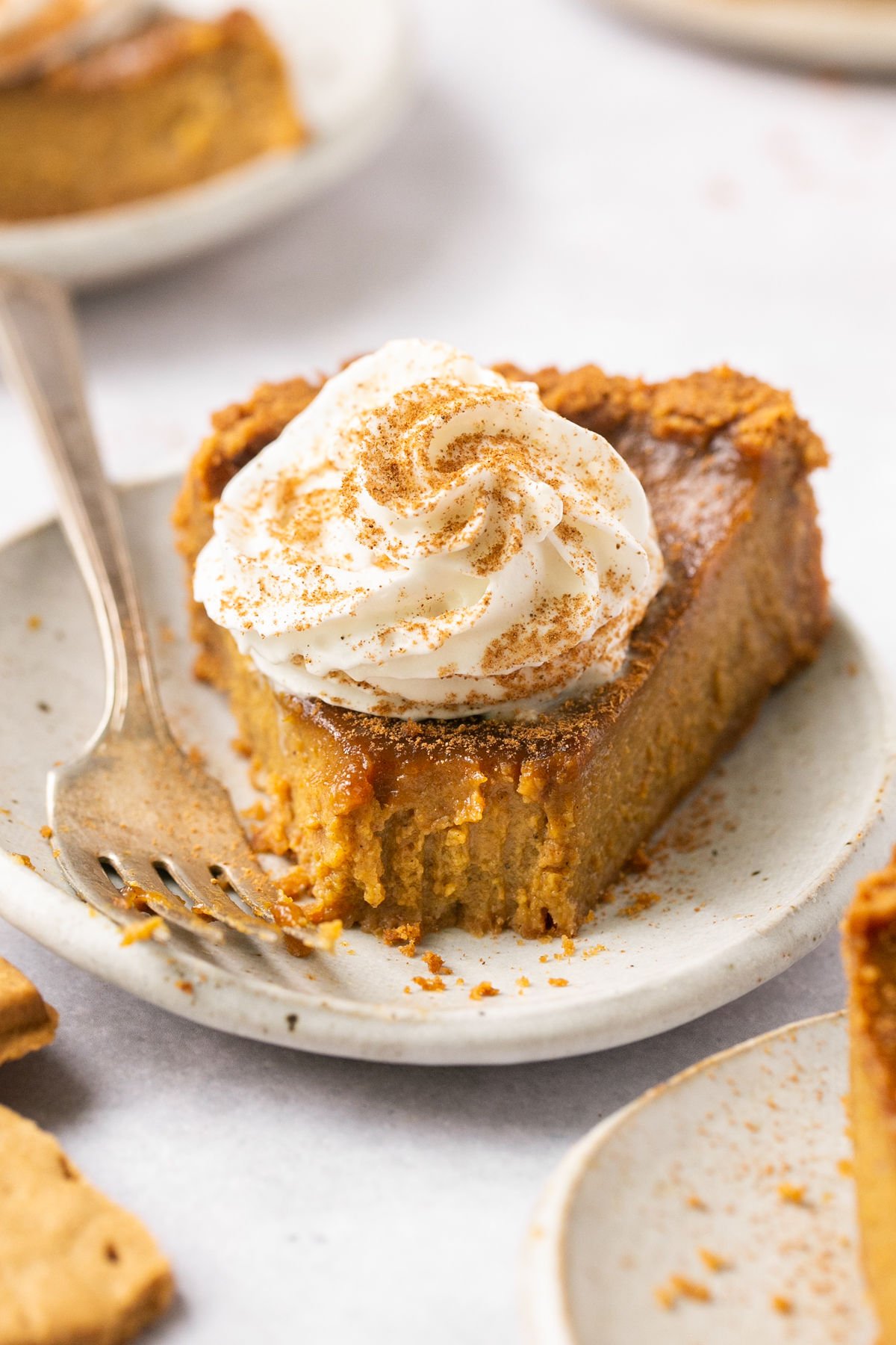 a closeup of a slice of gluten-free pumpkin pie with a graham cracker crust and a dollop of whipped cream on top. 
