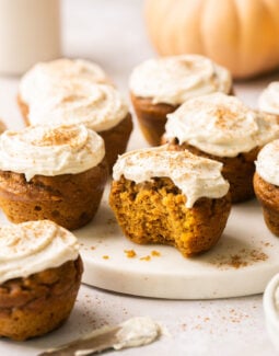 pumpkin muffins topped with cream cheese frosting and one has a bite taken out of it