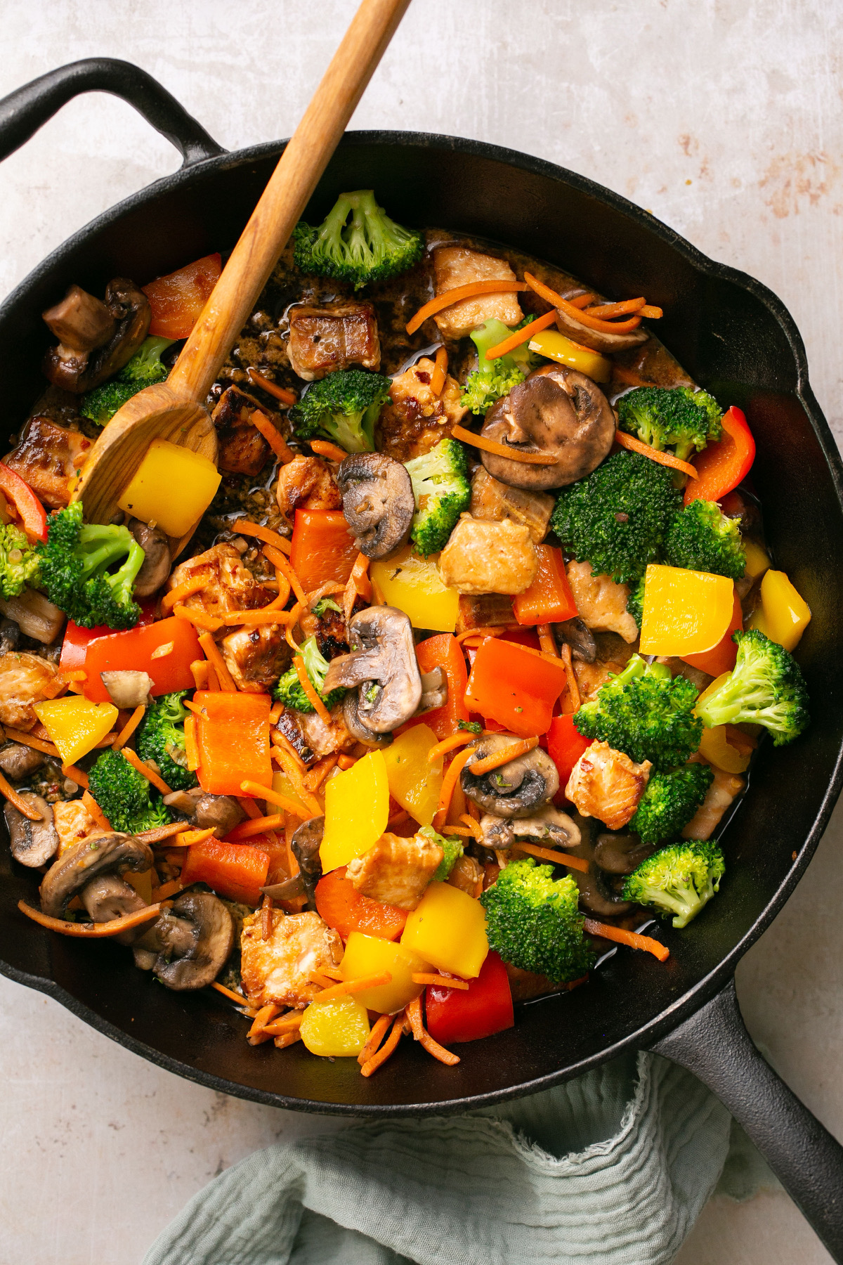 a closeup shot of a cast iron pan containing salmon, veggies, and stir fry sauce with a wooden spoon