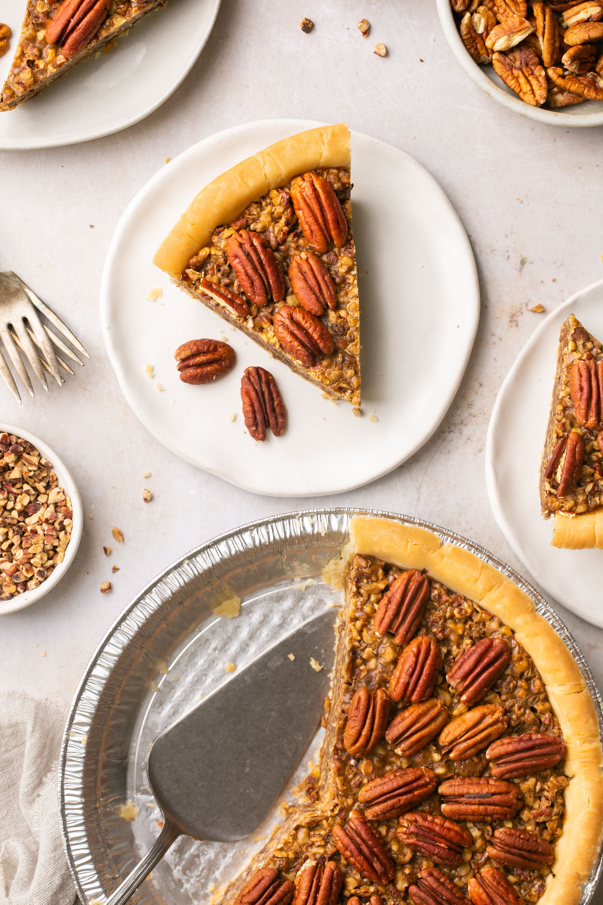 an overhead shot of a slice of pecan pie topped with pecan halves next to a foil pie plate with half of a pie eaten