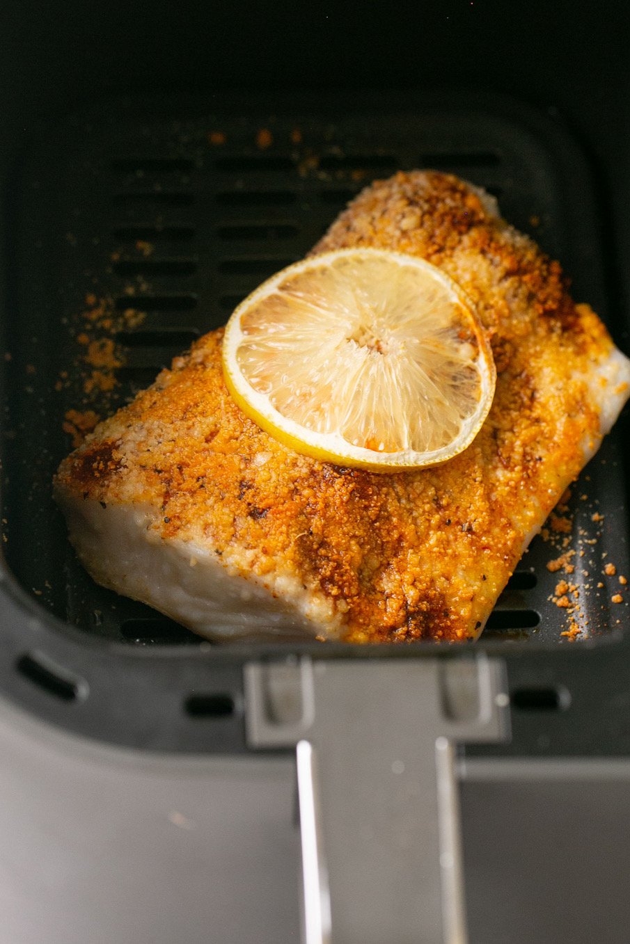 a photo of seasoned halibut with a lemon slice in an air fryer basket