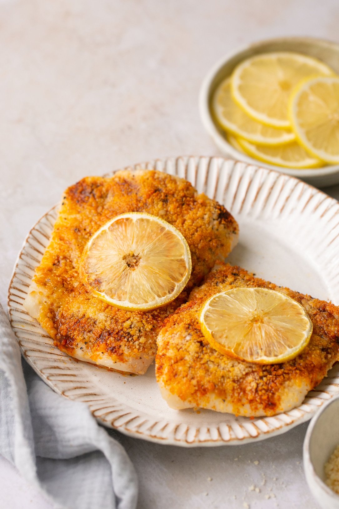 two halibut filets on a white plate topped with lemon slices