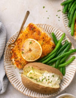 air fryer halibut on a plate with green beans and a baked potato with butter and sour cream