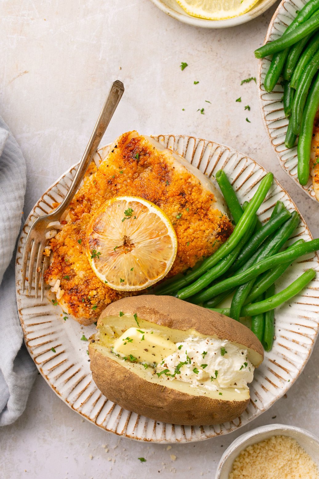 air fryer halibut on a plate with green beans and a baked potato with butter and sour cream