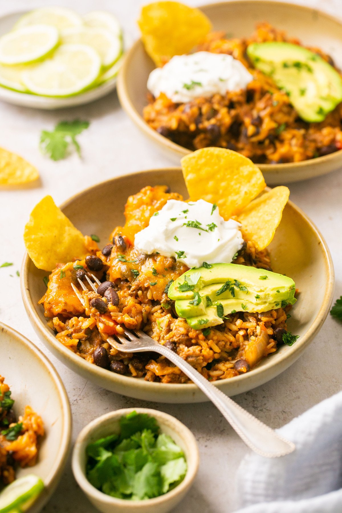 a bowl filled with taco in a bowl recipe fillings and topped with avocado, sour cream, and avocado with a silver fork resting on the side of the bowl. 