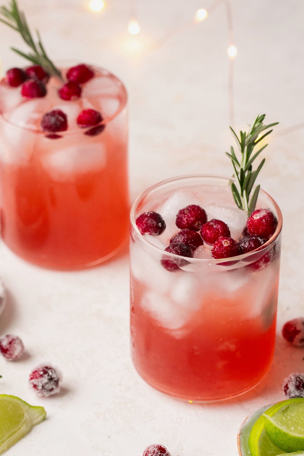 two cocktail glasses filled with mistletoe martini and topped with sugared cranberries and sprigs of rosemary