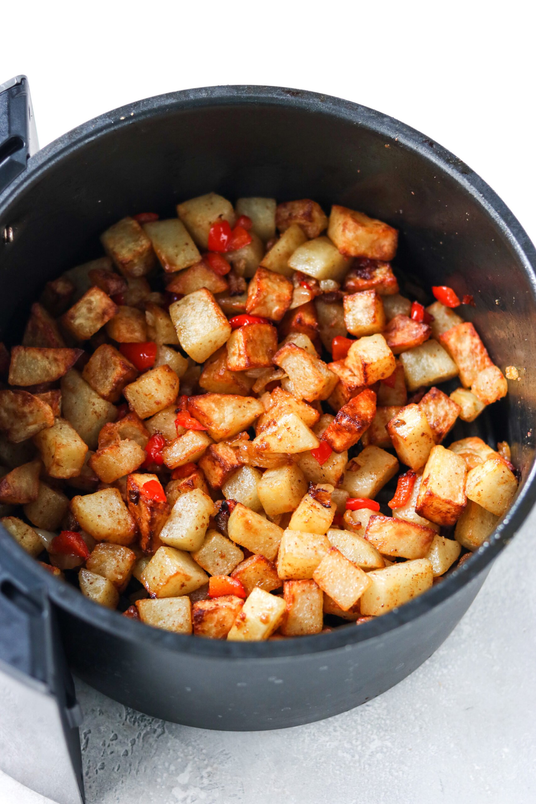 cubed potatoes with bell pepper and onion in an air fryer basket