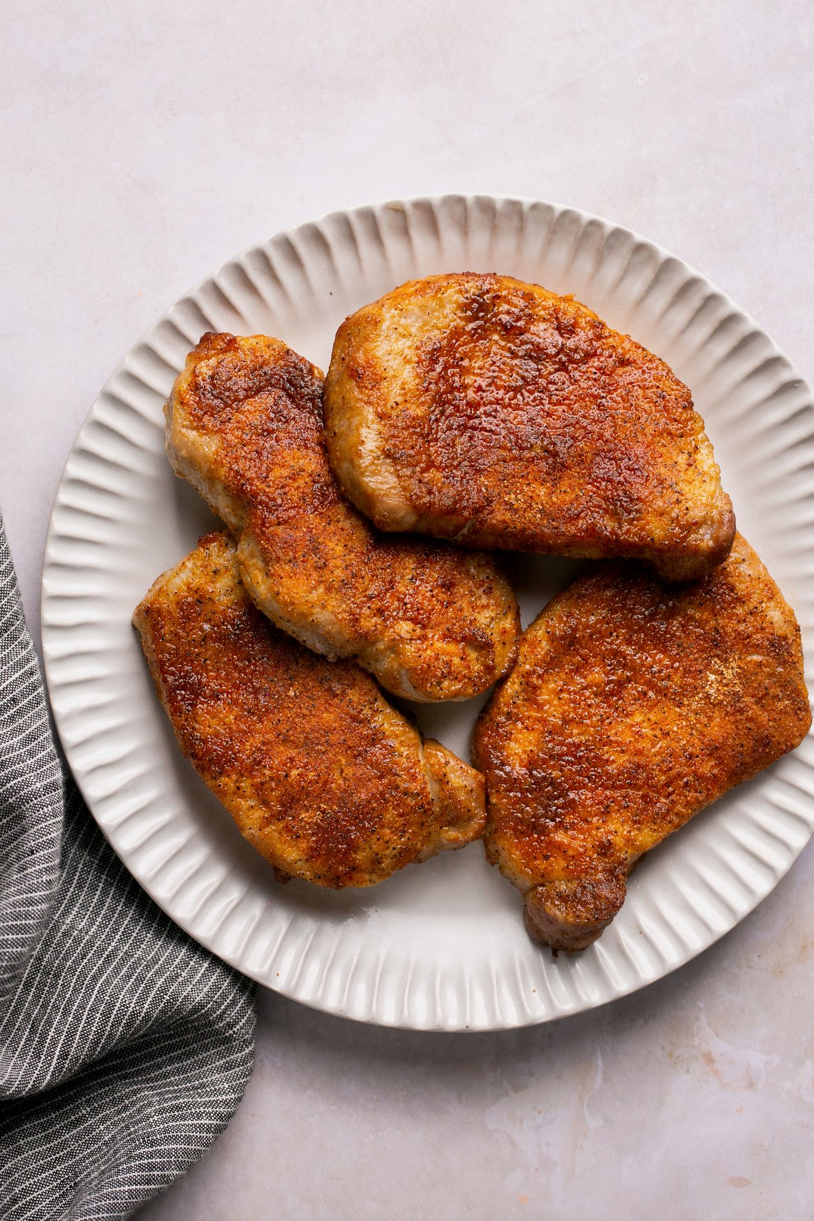 seasoned and cooked pork chops stacked on a white plate