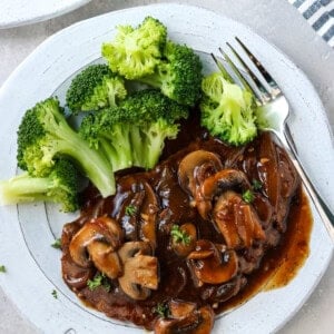cubed steak with mushrooms and onion gravy on a gray plate with steamed broccoli