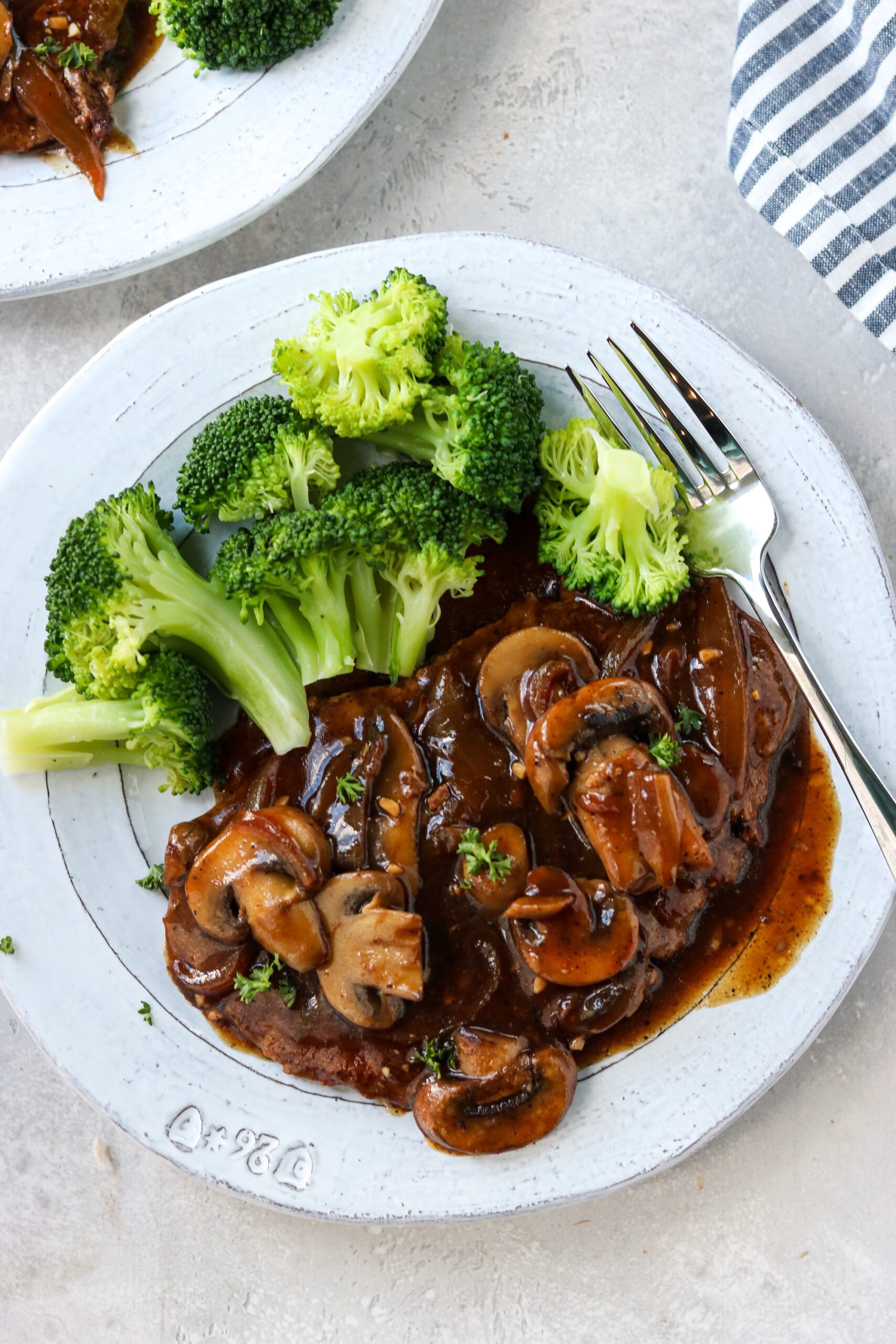 cubed steak with mushrooms and onion gravy on a gray plate with steamed broccoli