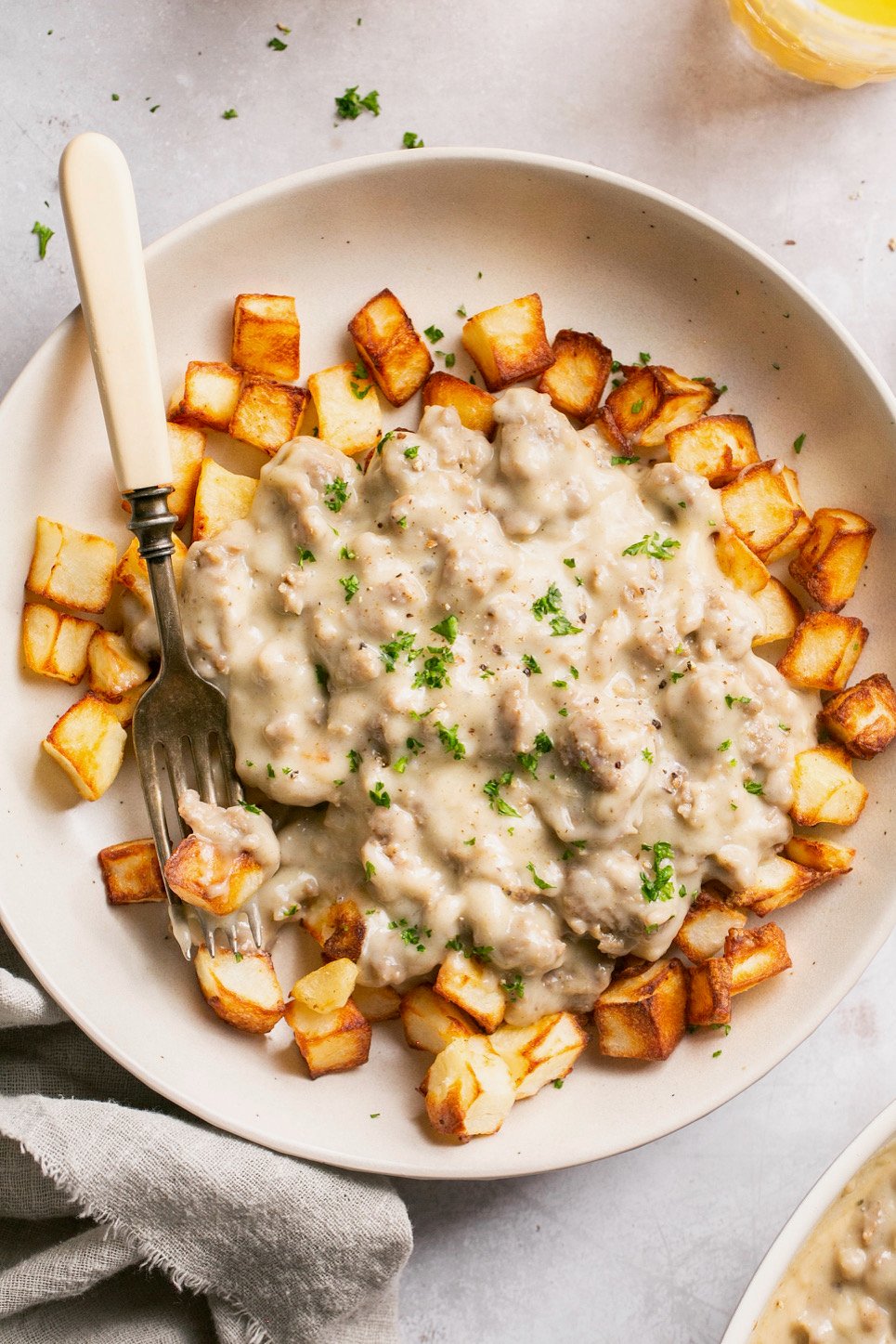 a closeup of sausage gravy smothered on top of crispy potatoes with fork resting on the side. 