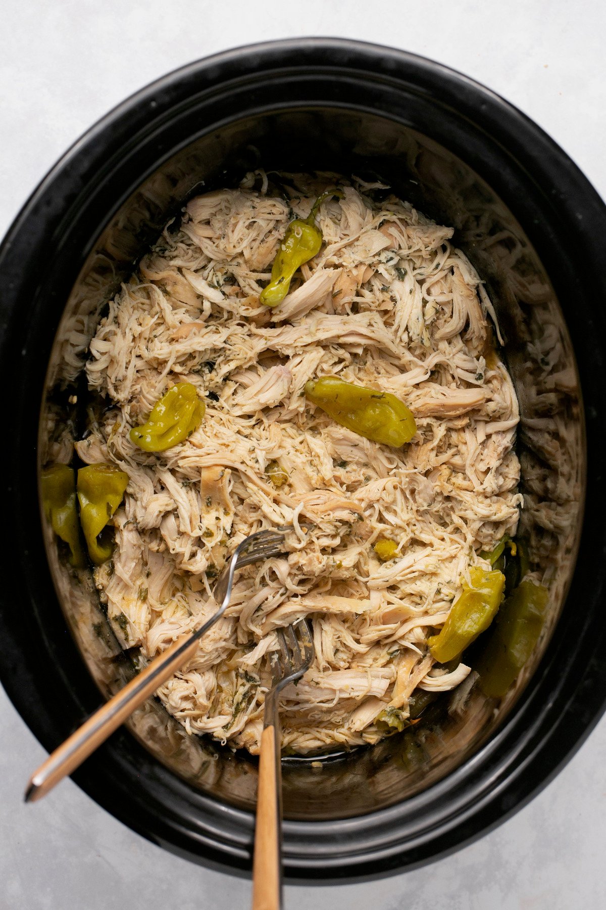 a crock pot filled with Mississippi chicken and pepperoncini peppers